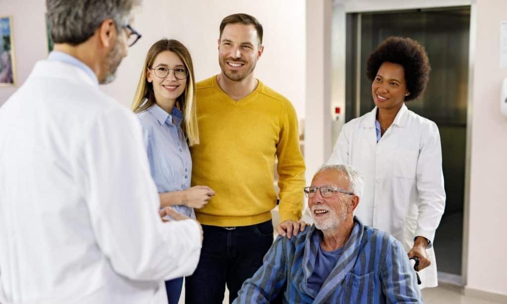 Doctor speaking with family in a hospital hallway; older man in wheelchair.