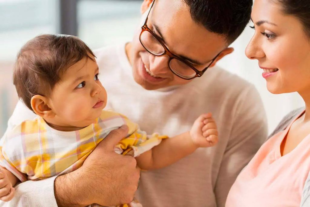 Man holding baby, looking at baby; woman looking at baby; all smiling.