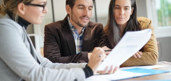 A woman in glasses reviews a document with a couple. They are in an office setting.