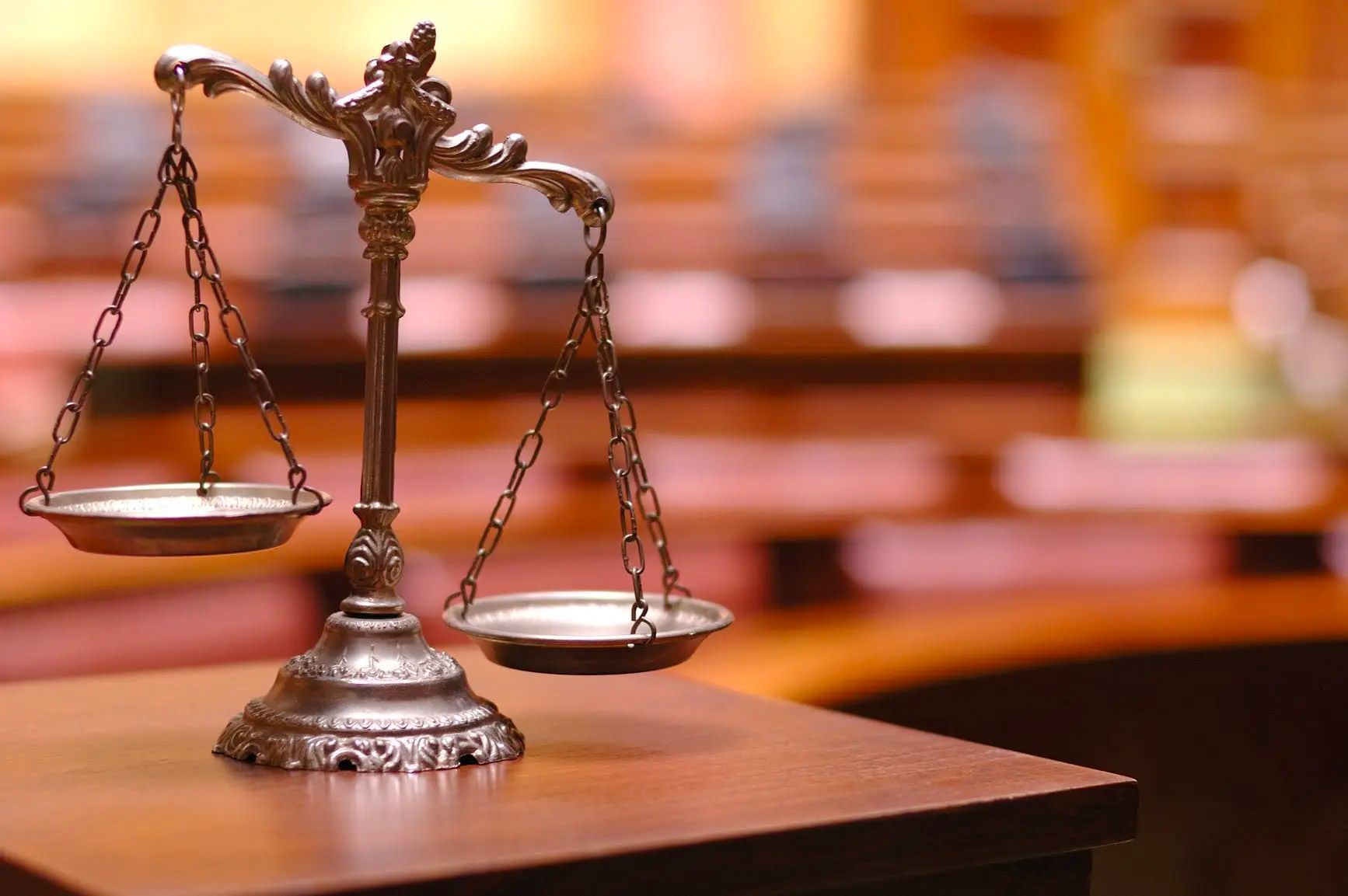 Scales of justice on a wooden surface in a courtroom setting.