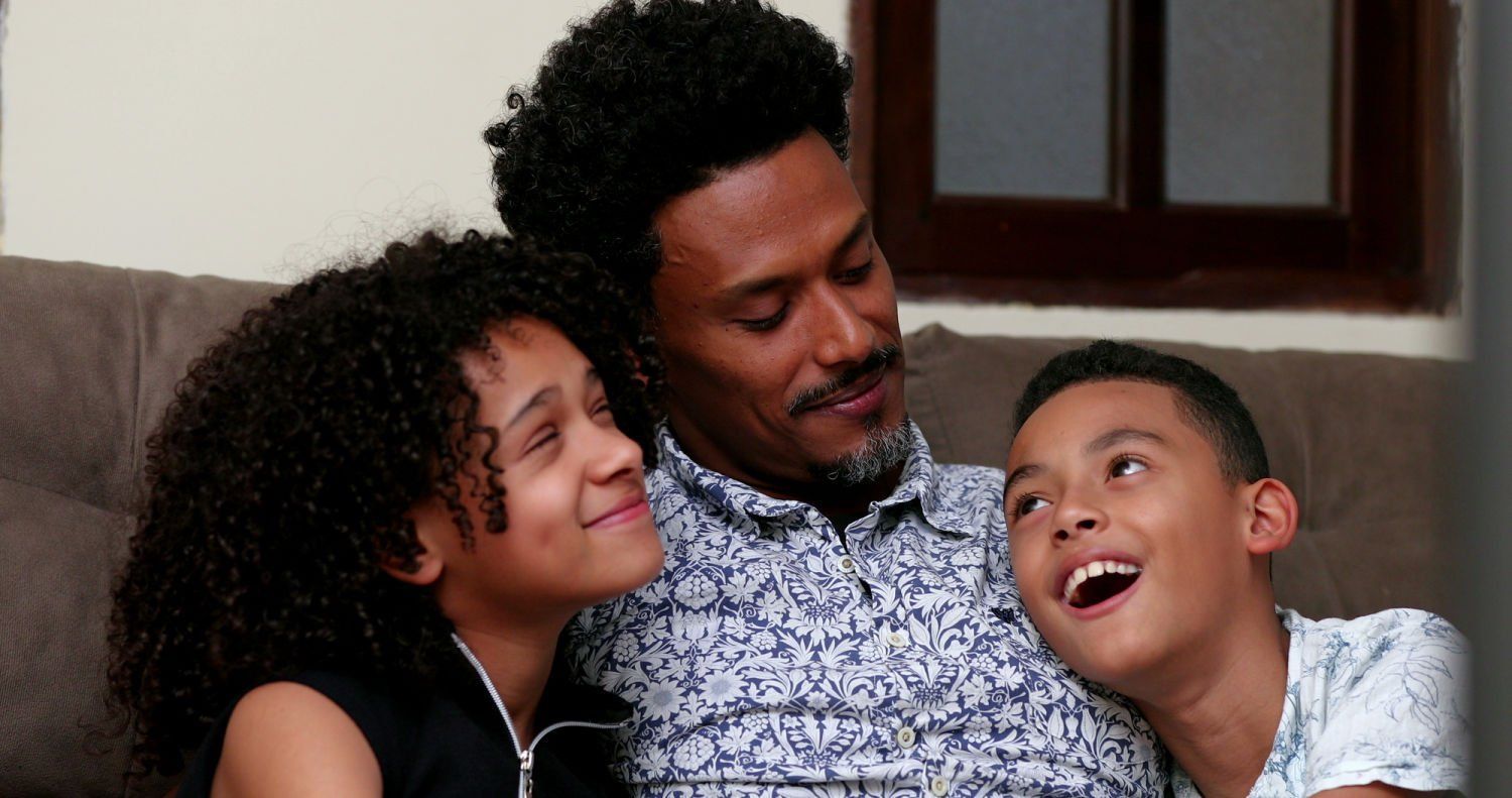 Father and two children on a couch, smiling and looking at something.