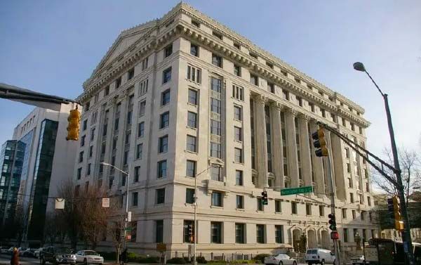Large, light-colored courthouse with columns, windows, and street signs in an urban setting.