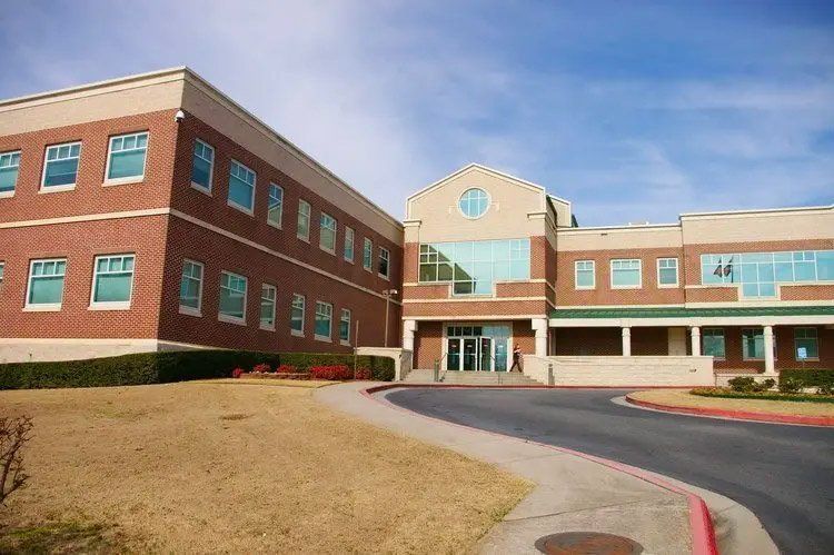 Brick building with multi-pane windows and a curved driveway under a blue sky.