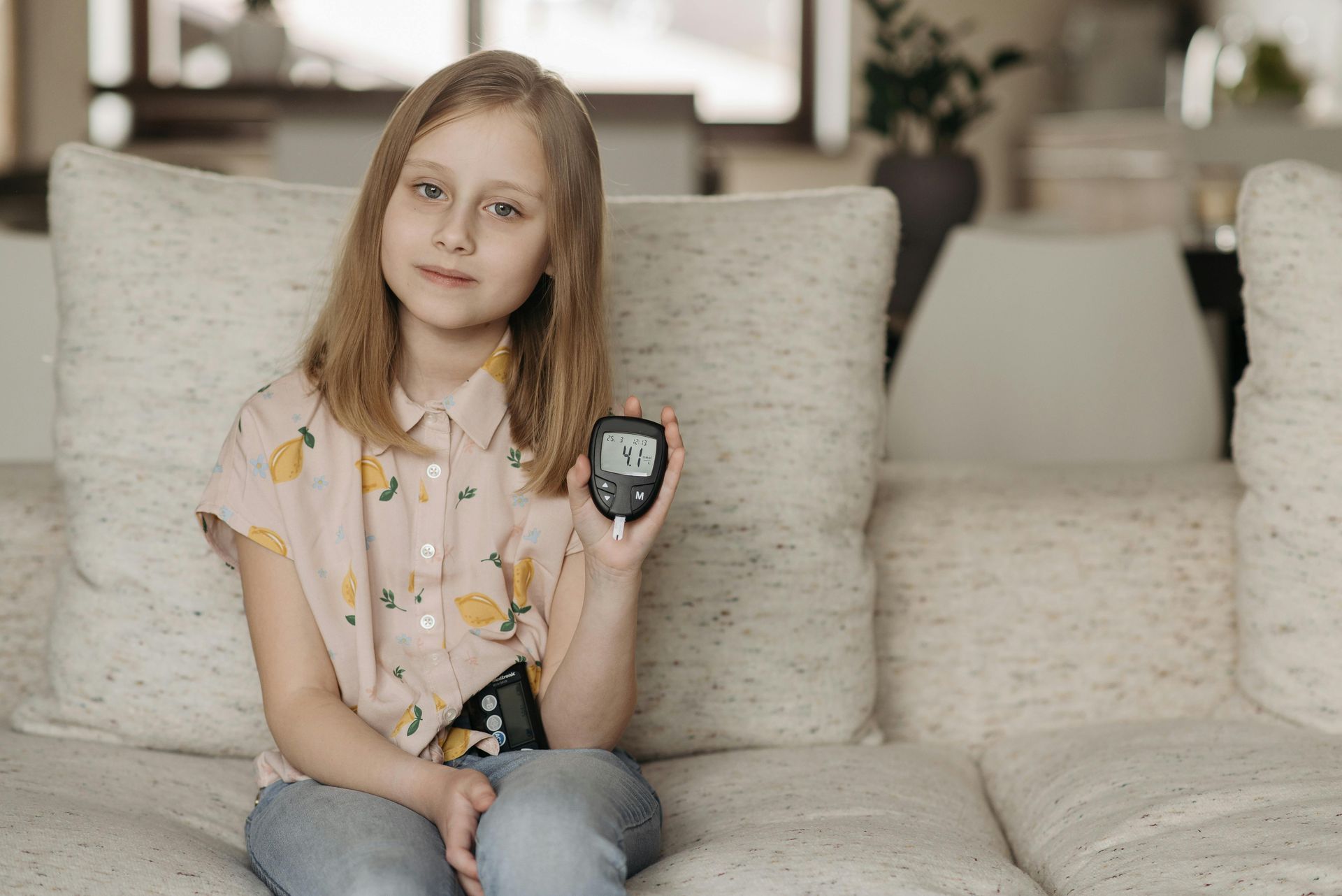 Girl holding blood glucose monitor, sitting on a sofa, inside.