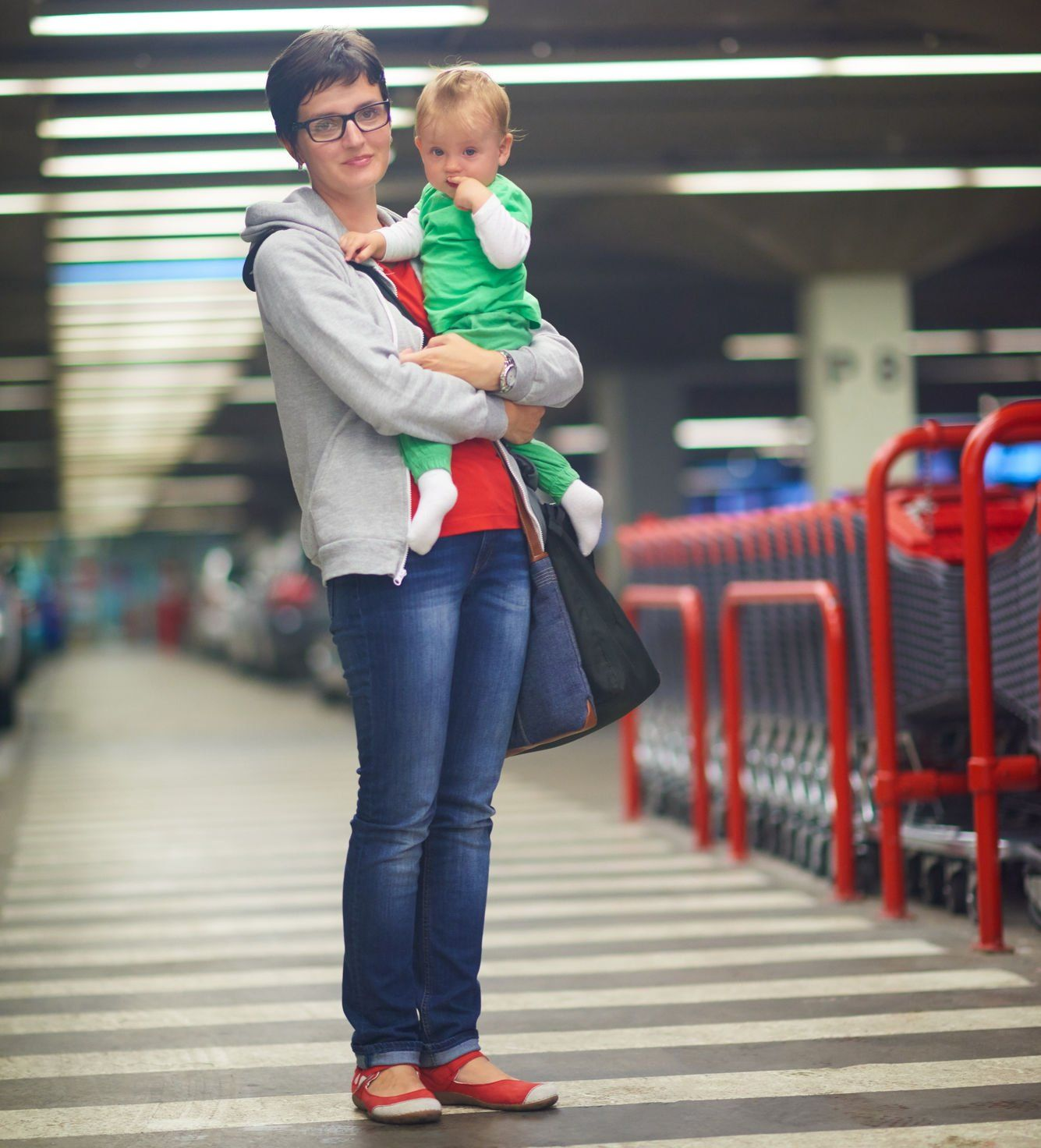 Woman holding a baby in a parking garage. The baby has a finger in its mouth.