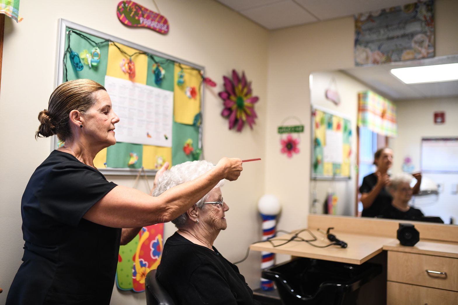 Caregiver helping a resident with hair styling inside Bellamy Assisted Living salon