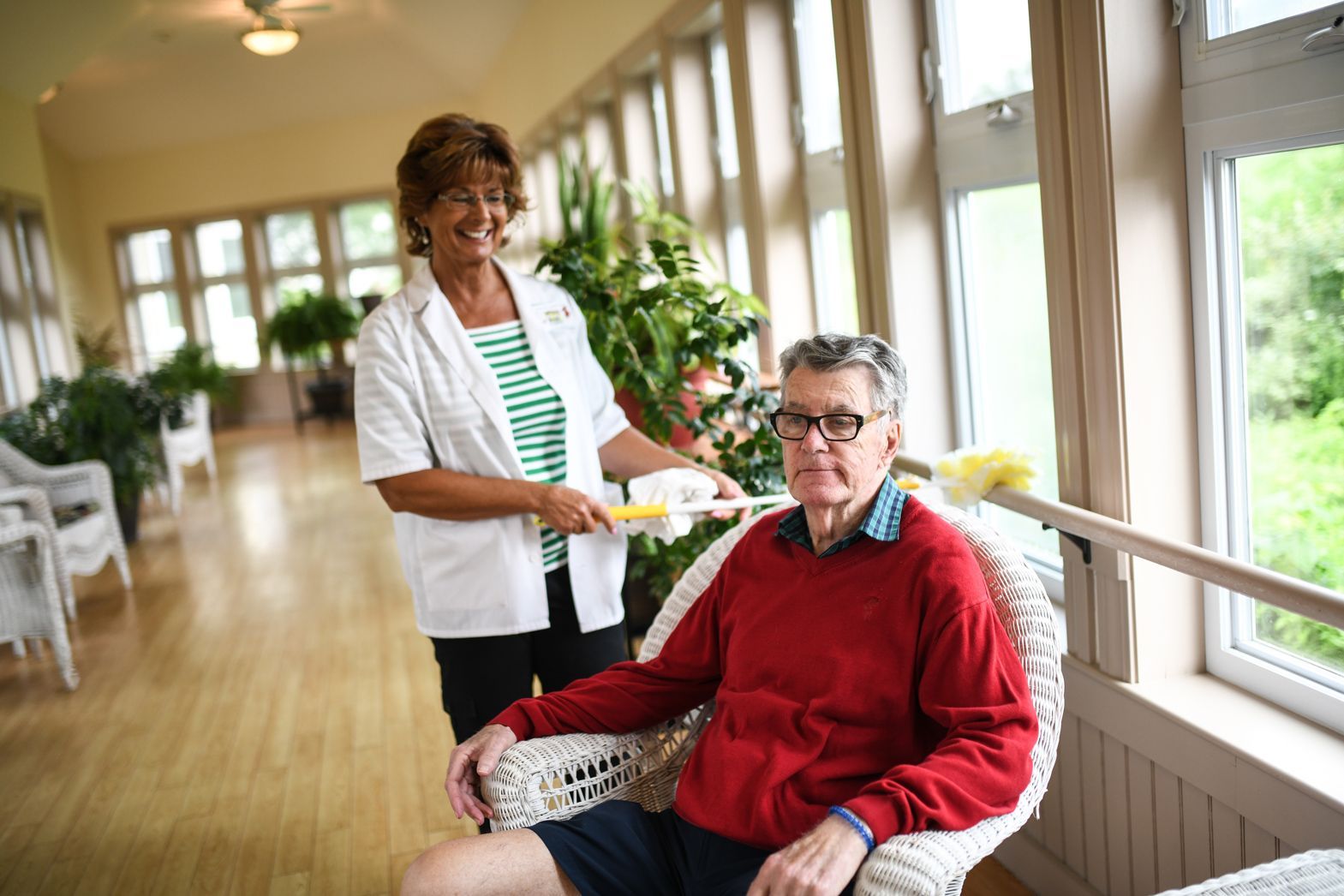 Caregiver and resident smiling in a sunlit hallway at Bellamy Assisted Living