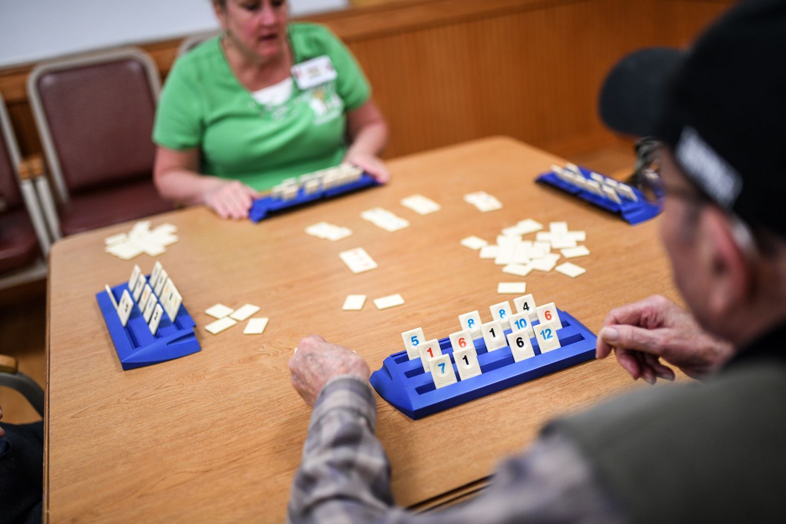 Residents playing Rummikub at a wooden table in Bellamy Assisted Living game room