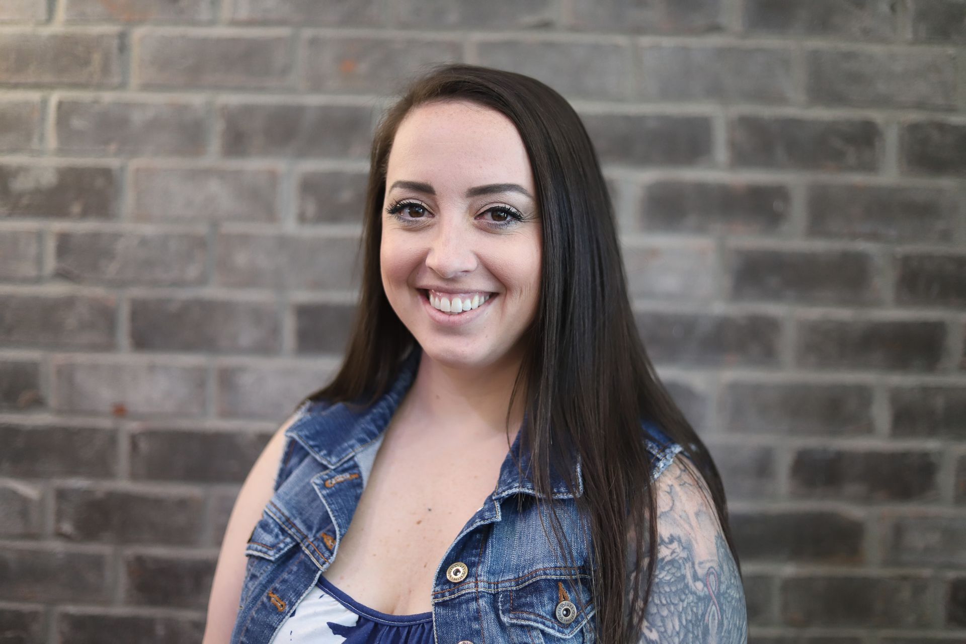 A woman is smiling in front of a brick wall.