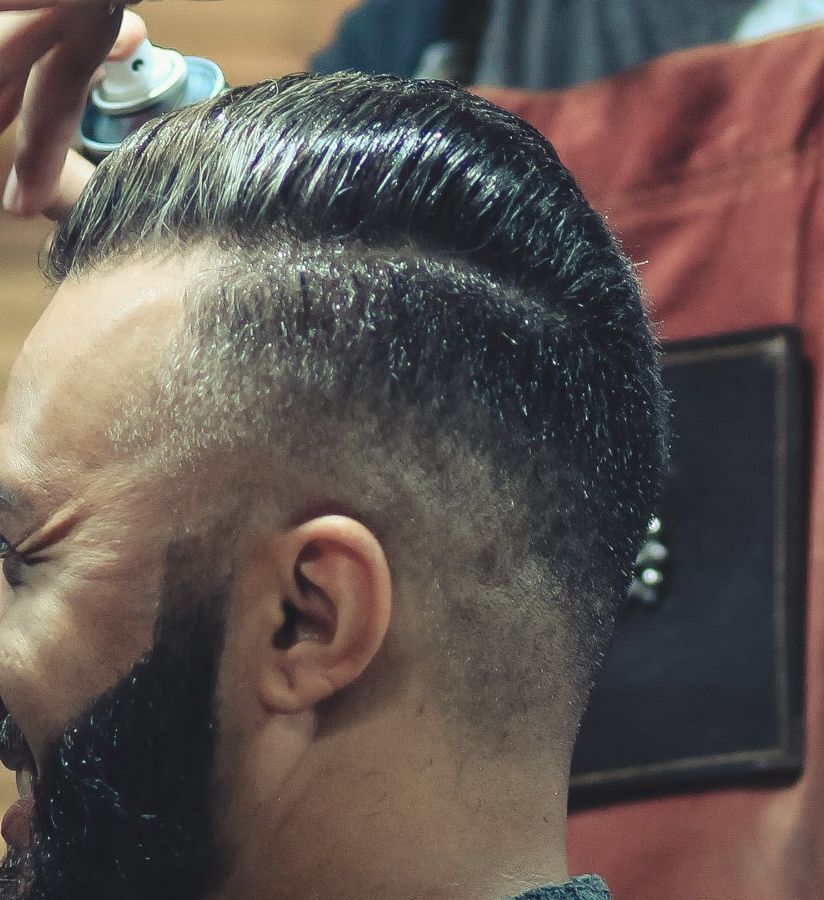 A man with a beard is getting his hair sprayed