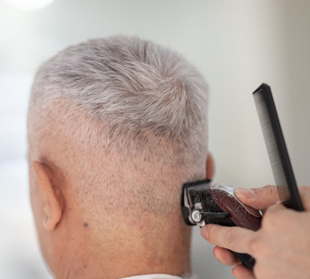 An older man is getting his hair cut by a barber.