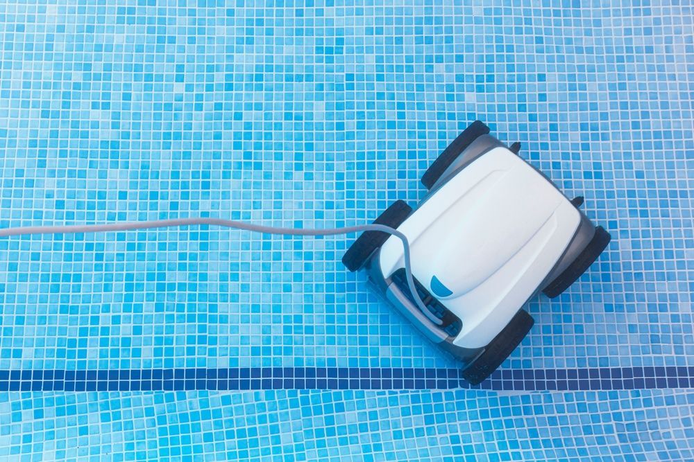 Robotic pool cleaner on blue mosaic tiles, with cord trailing across the pool floor