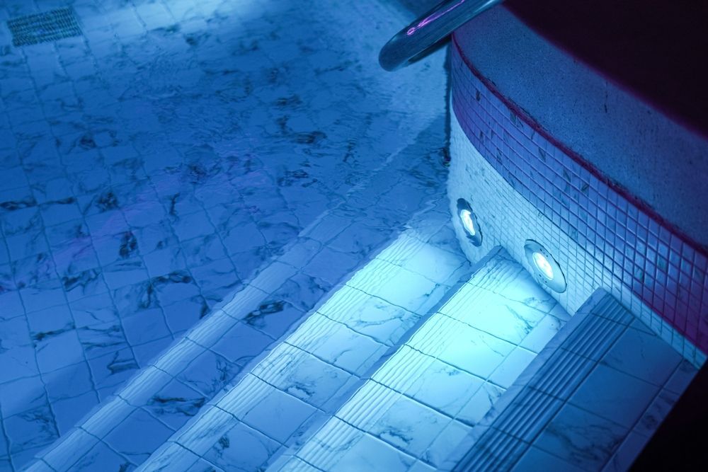Blue-lit airplane cockpit windows and fuselage at night, viewed from above on the tarmac
