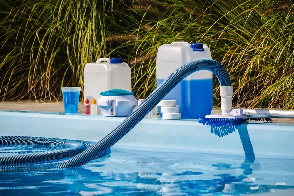 Pool cleaning supplies beside a swimming pool, with a vacuum hose in the water