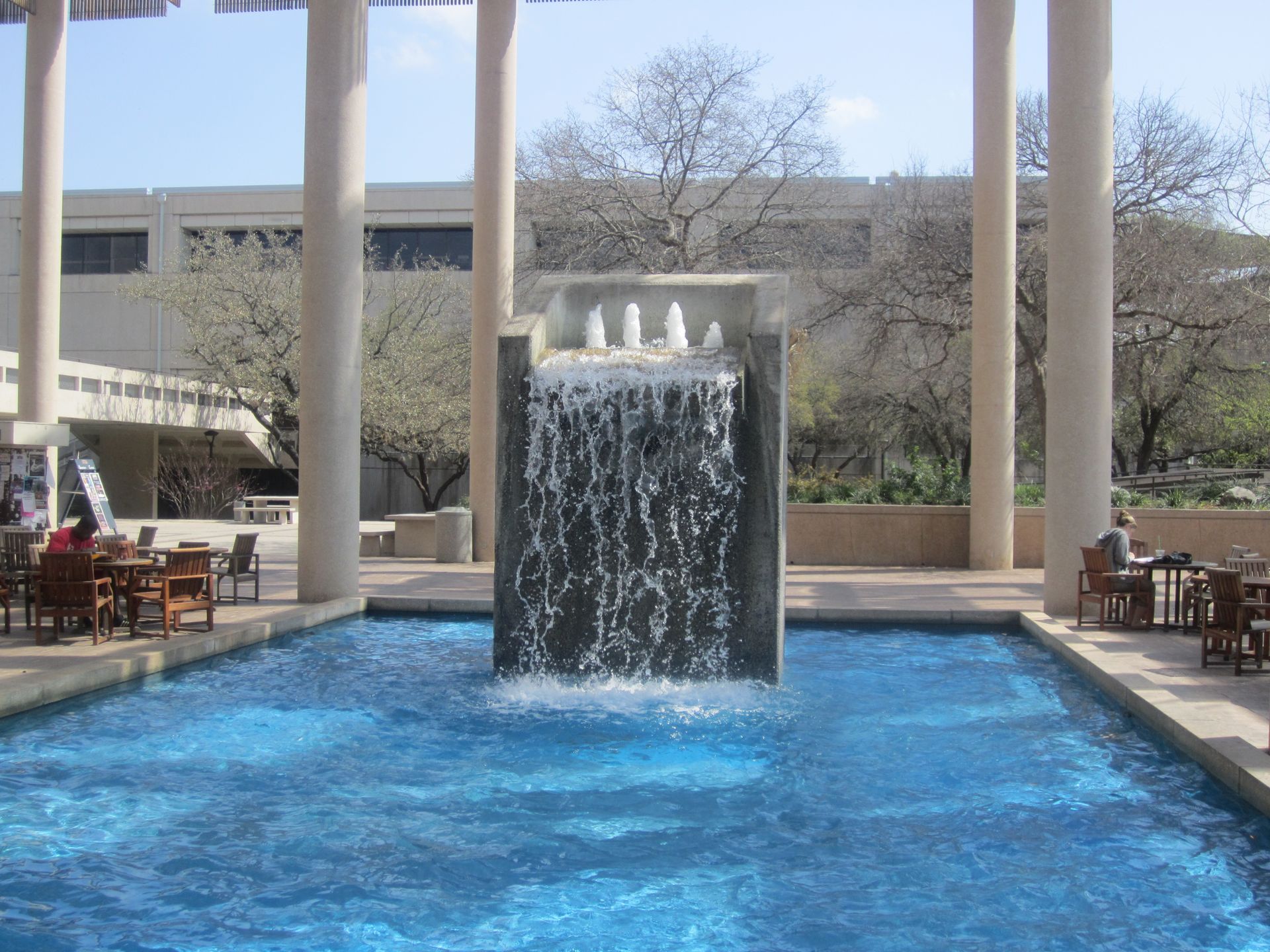 Outdoor fountain with a central water feature in a blue pool, framed by trees and patio seating