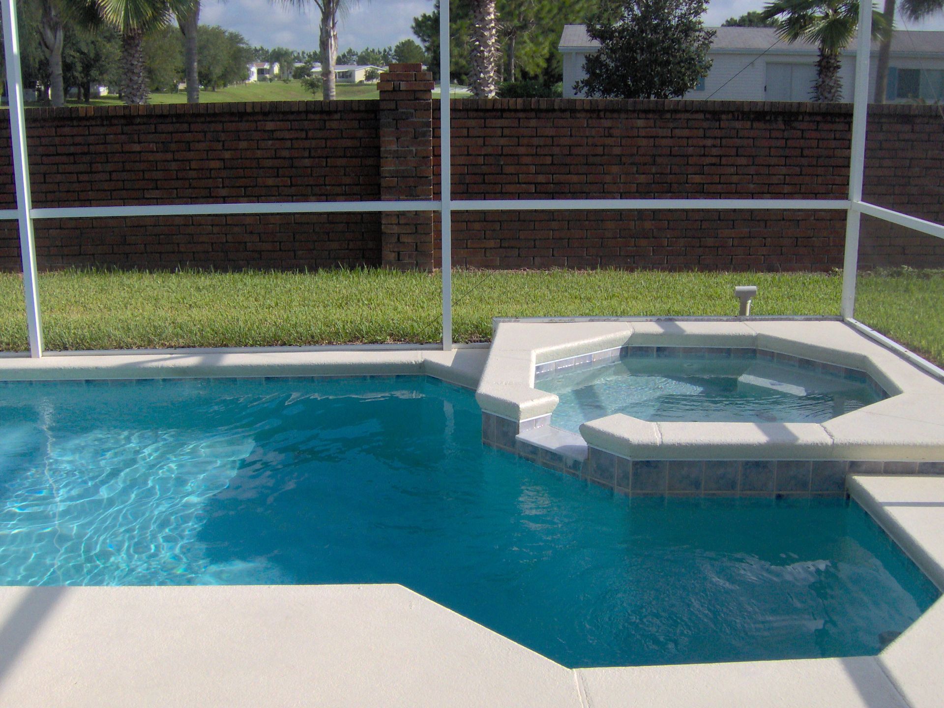 Blue swimming pool beside a hot tub with a brick wall and screened backyard in the background