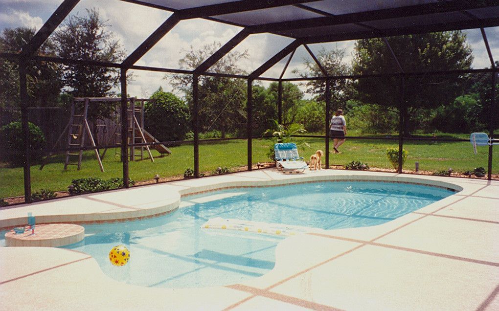 Screened-in backyard pool with blue water, patio chairs, and green lawn beyond