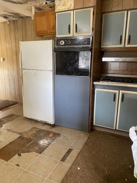 Dated kitchen with white fridge, gray oven, blue cabinets, and worn floor tiles.