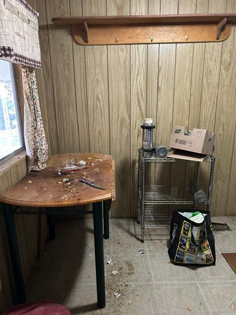 Small wood-paneled room with a table, metal rack, lantern, and bag on the floor.
