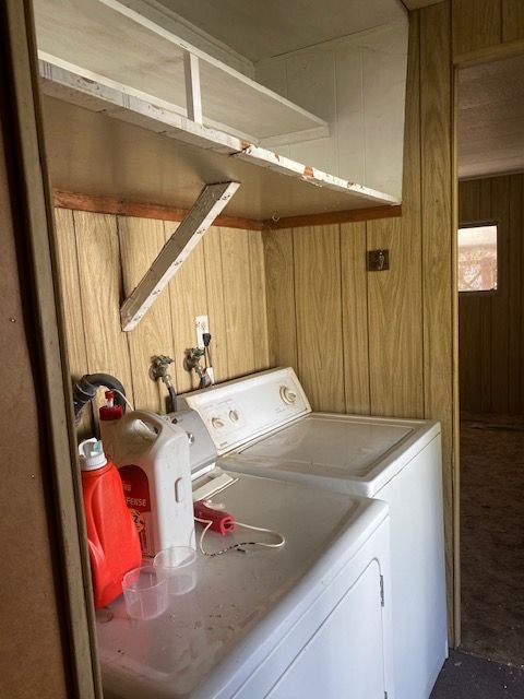 Laundry room with white washer and dryer, wood-paneled walls, and shelves above.