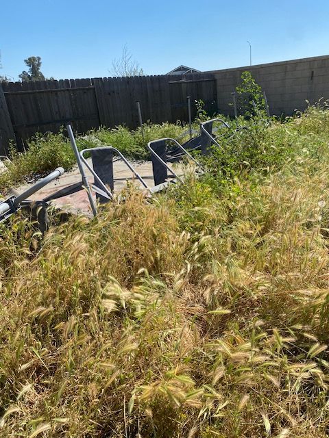 Overgrown backyard with a toppled metal patio table and chairs near a wooden fence