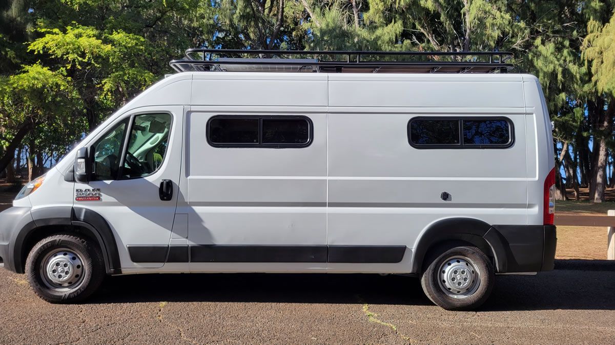 A white van with a roof rack is parked on the side of the road.