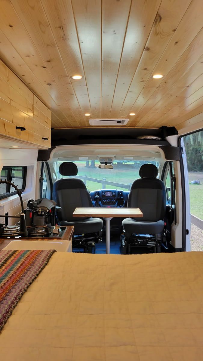 Interior view of a camper van conversion with wood ceiling, compact kitchen setup, and front swivel seats with table—ideal for road trips and van life travel in Maui.