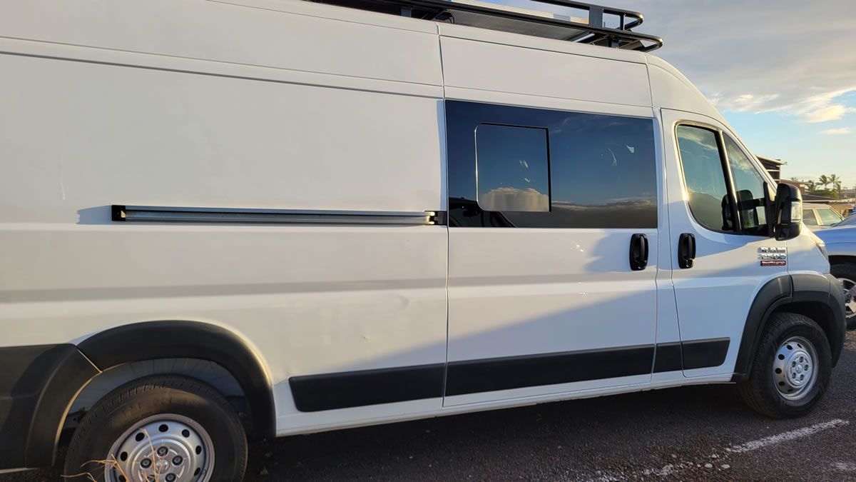 A white van with a roof rack is parked in a parking lot.