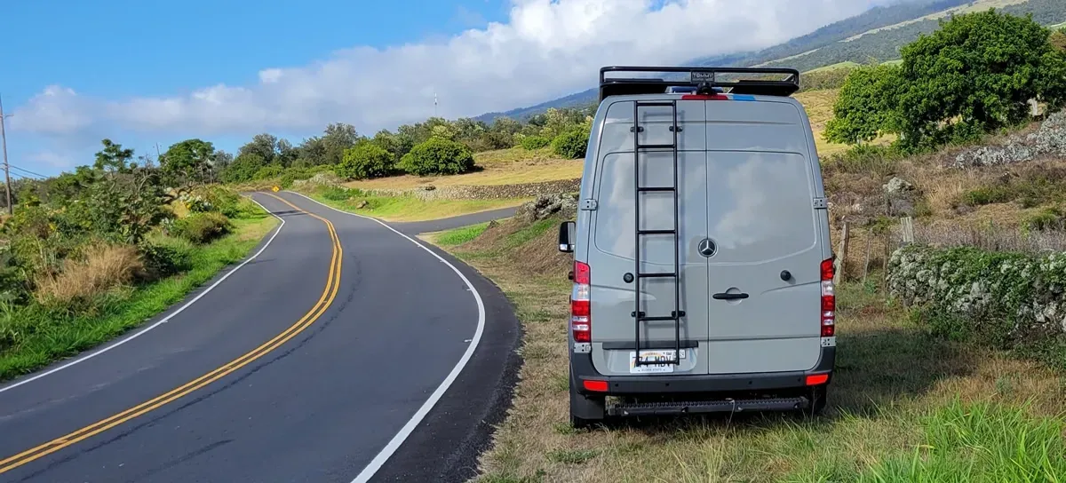 A white van with a ladder on the back is parked on the side of a road.