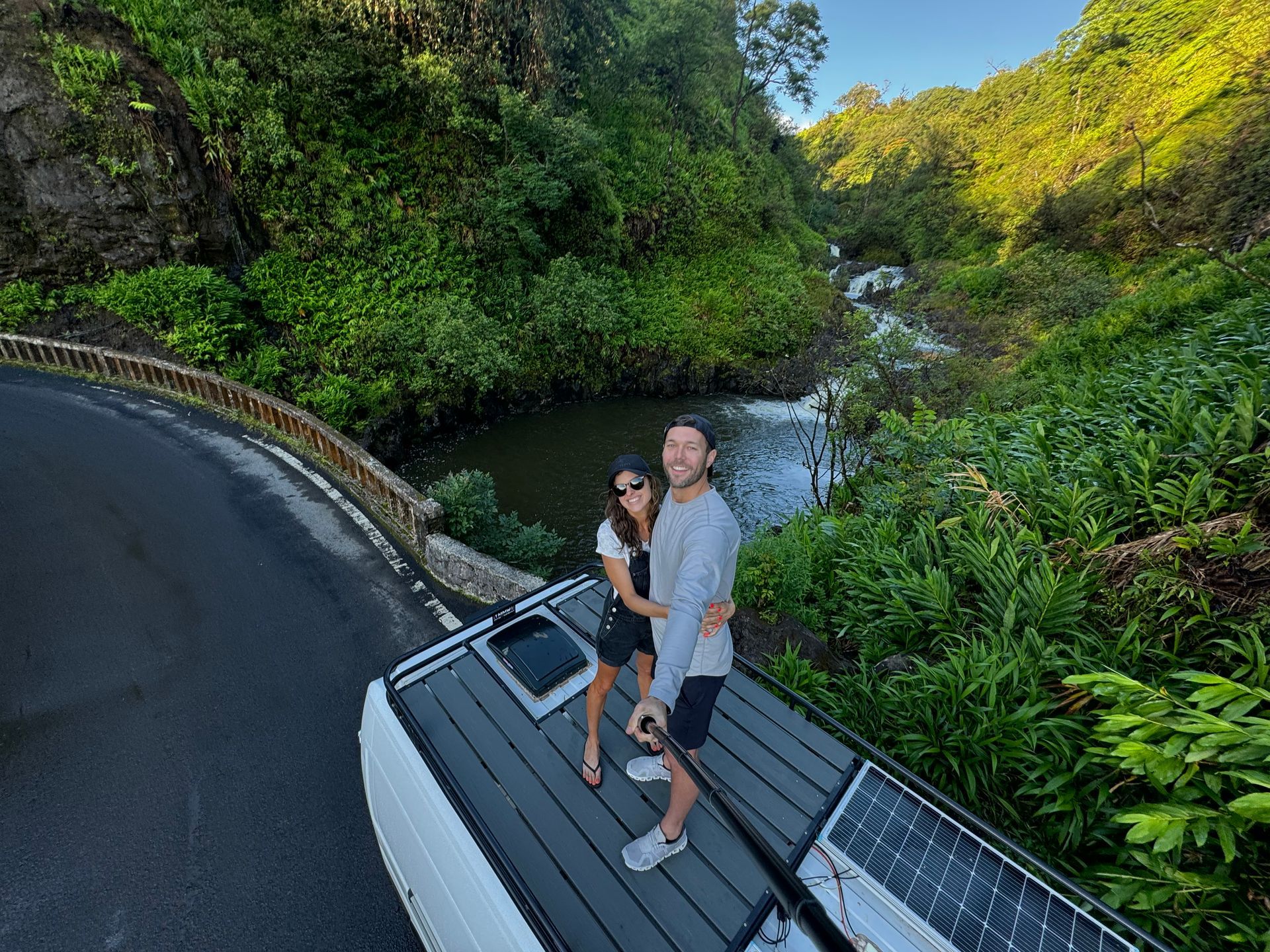 A man and a woman are standing on the roof of a van next to a river.