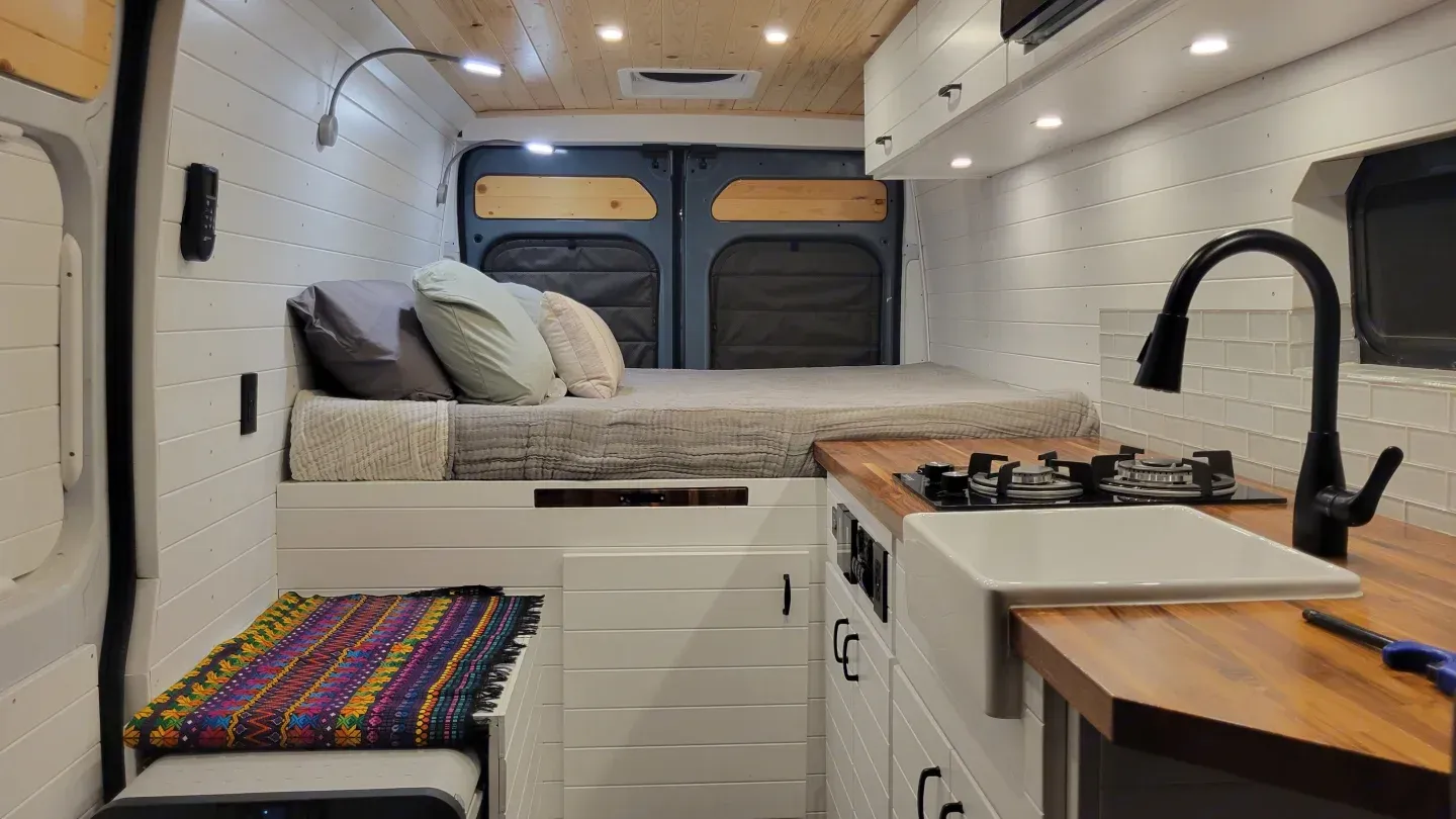The inside of a van with a bed and a sink.