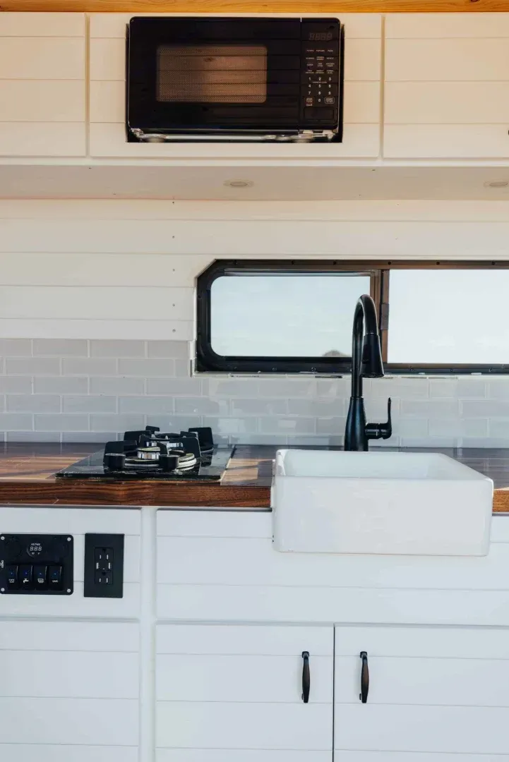 A kitchen with a sink , stove , microwave and window.