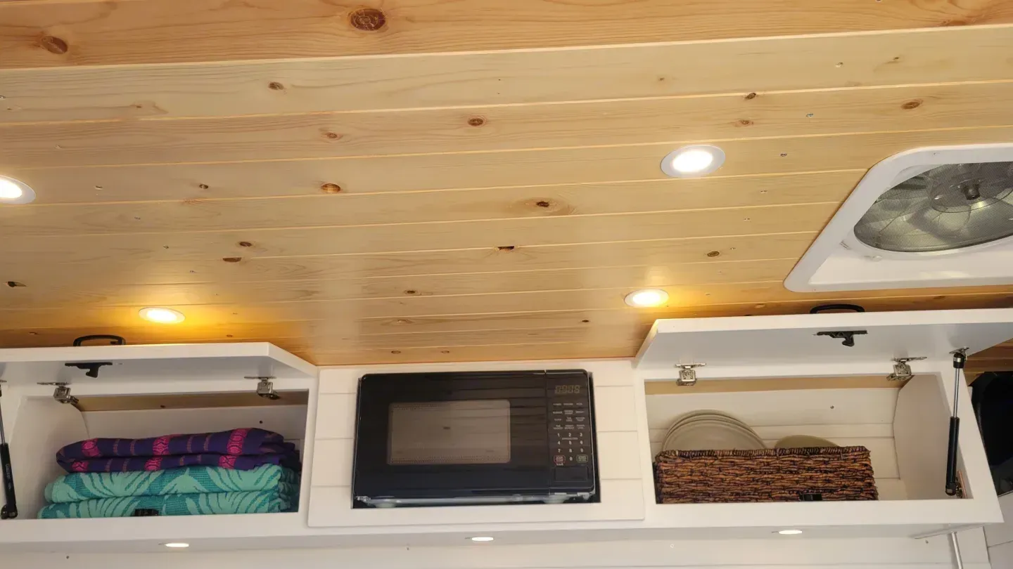 A kitchen with a microwave and a fan on the ceiling.