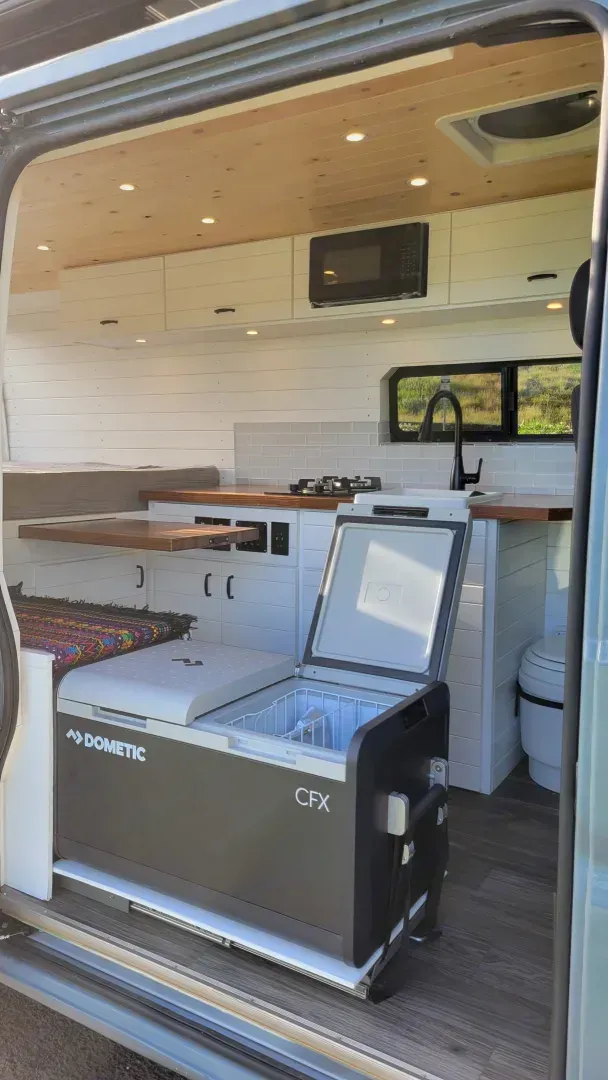 The inside of a van with the door open and a fridge in the back.