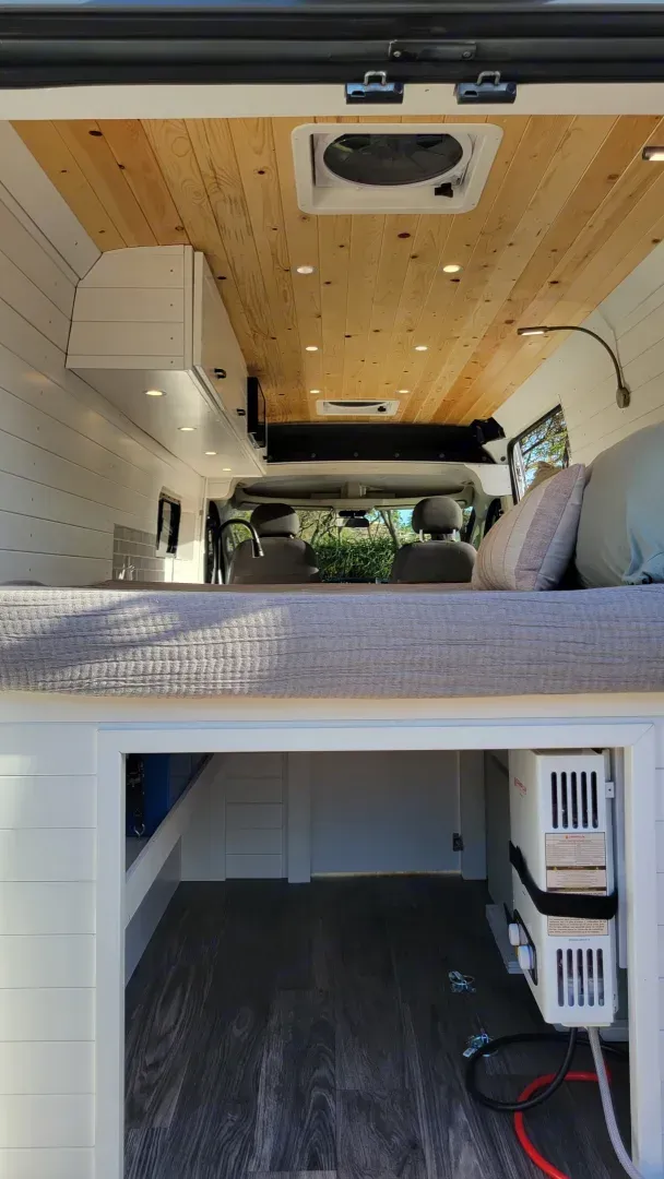 The inside of a van with a bed and a fan on the ceiling.