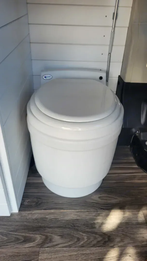 A white toilet is sitting on a wooden floor in a bathroom.