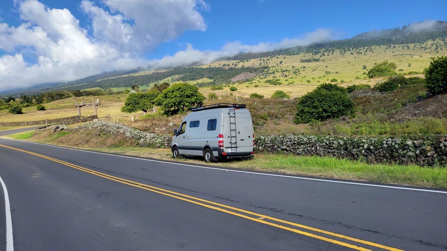 Sprinter camper van driving on scenic highway with blue skies available for rental by Mana Vans in ʻUlupalakua, Maui, HI.