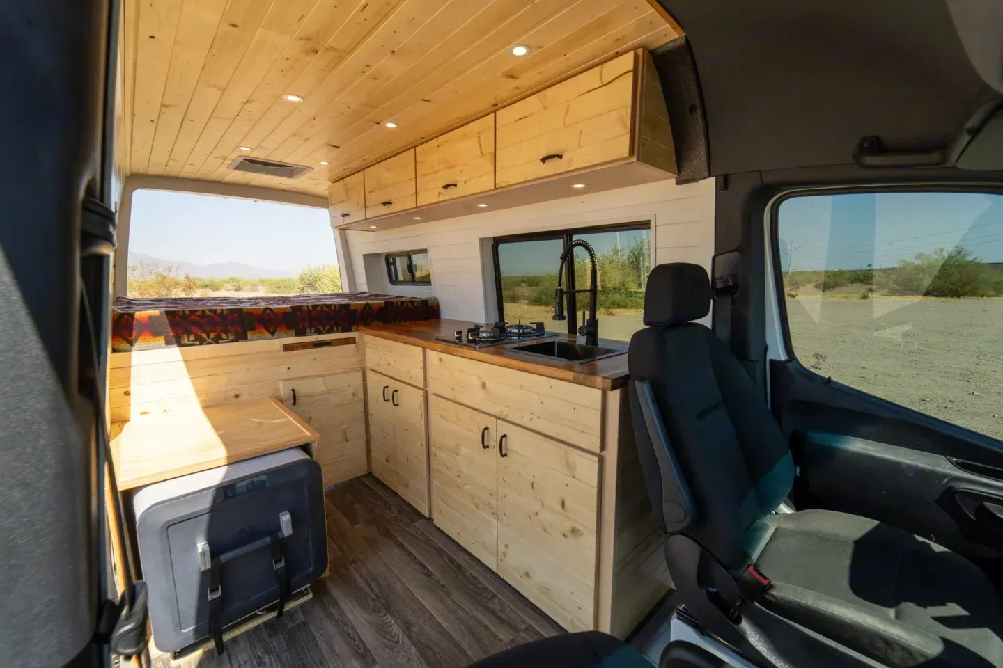 The inside of a Mercedes Benz camper van with wooden cabinets and a sink.
