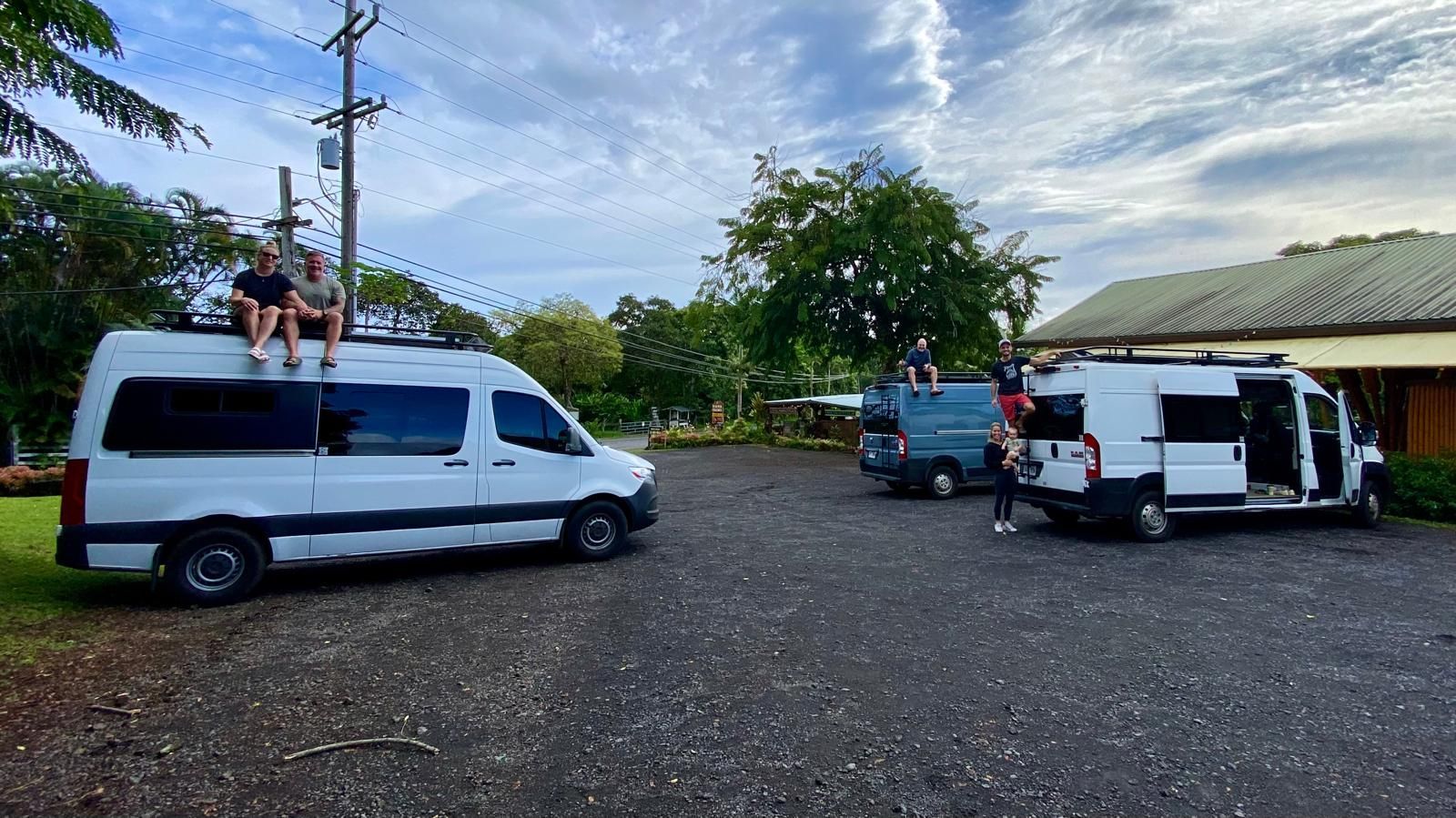 Three vans are parked in a parking lot with people sitting on top of them.