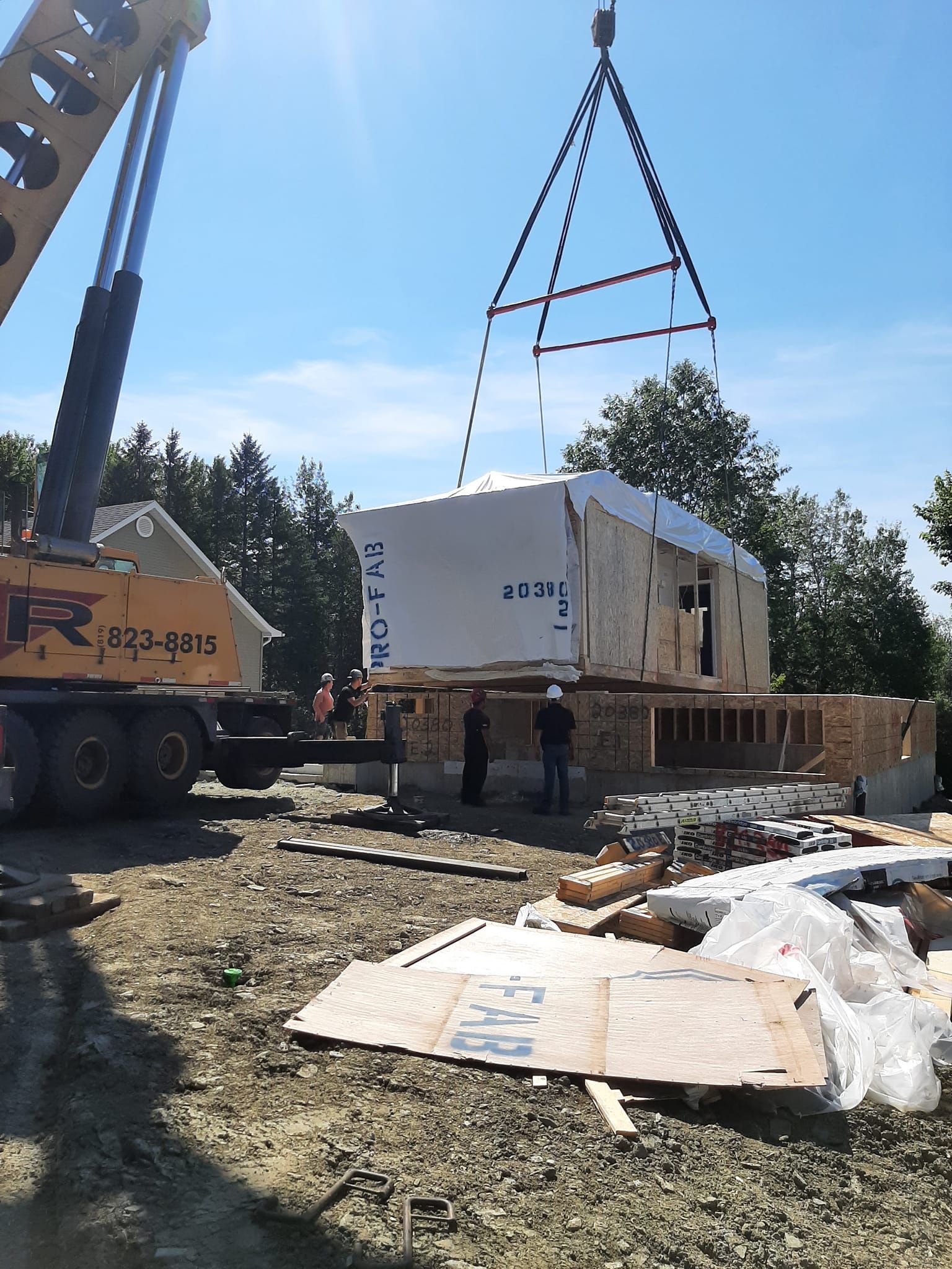 Une grue soulève la structure d'une maison modulaire sur ses fondations, sur un chantier de construction.