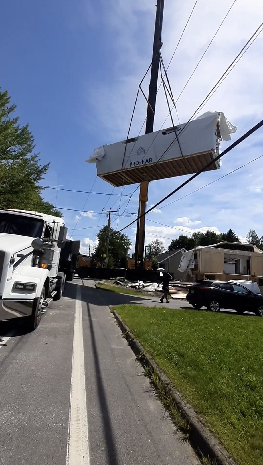 Une grue soulève une petite maison blanche et la dépose sur un camion plateau au bord d'une rue de banlieue.