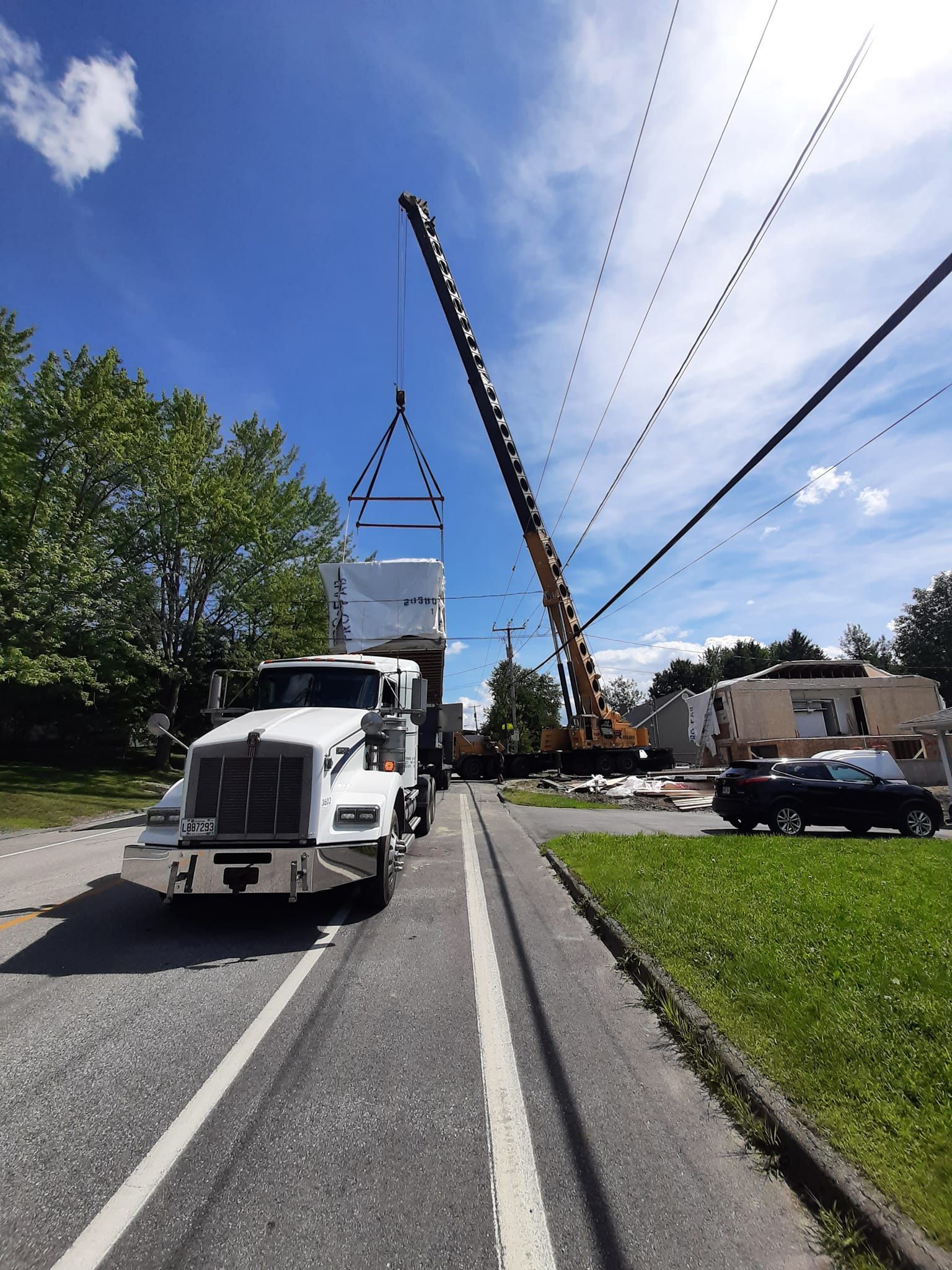 Un camion utilitaire soulève des lignes électriques dans une rue de banlieue sous un ciel bleu.