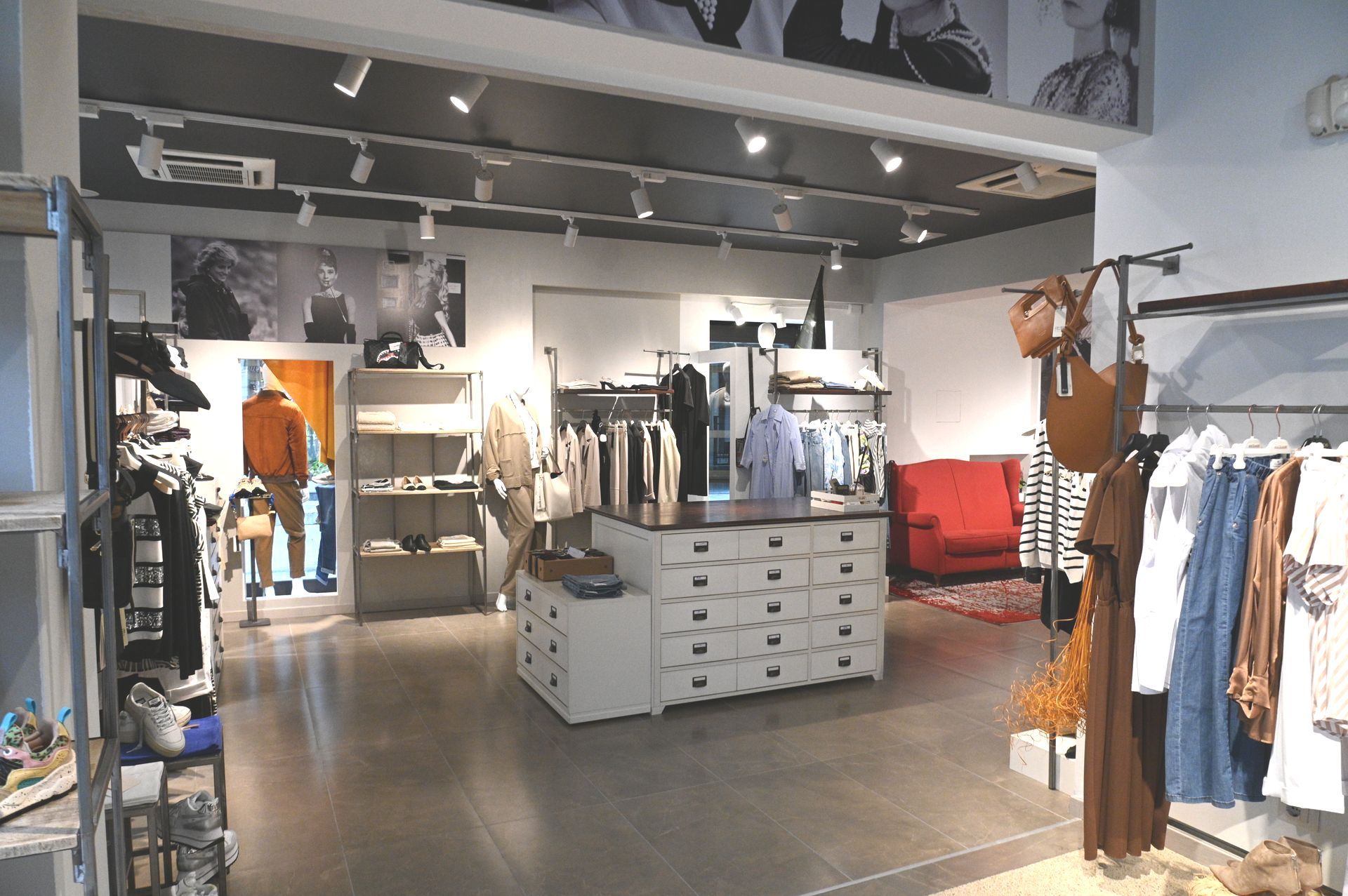 Interno di un negozio di abbigliamento, espositori con vari capi di abbigliamento, tavoli espositivi e un divano rosso.