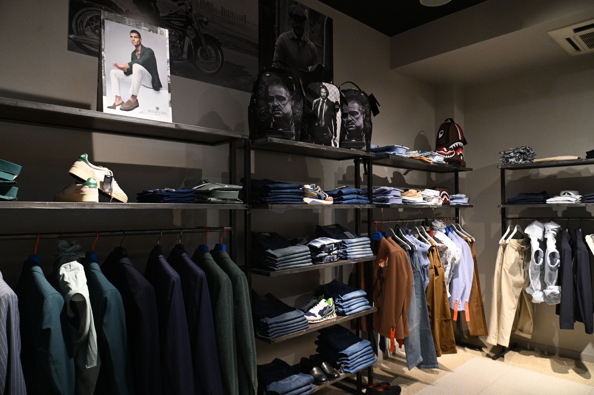 Interno di un negozio di abbigliamento con scaffali che espongono jeans, camicie e accessori; manichini che indossano abiti.