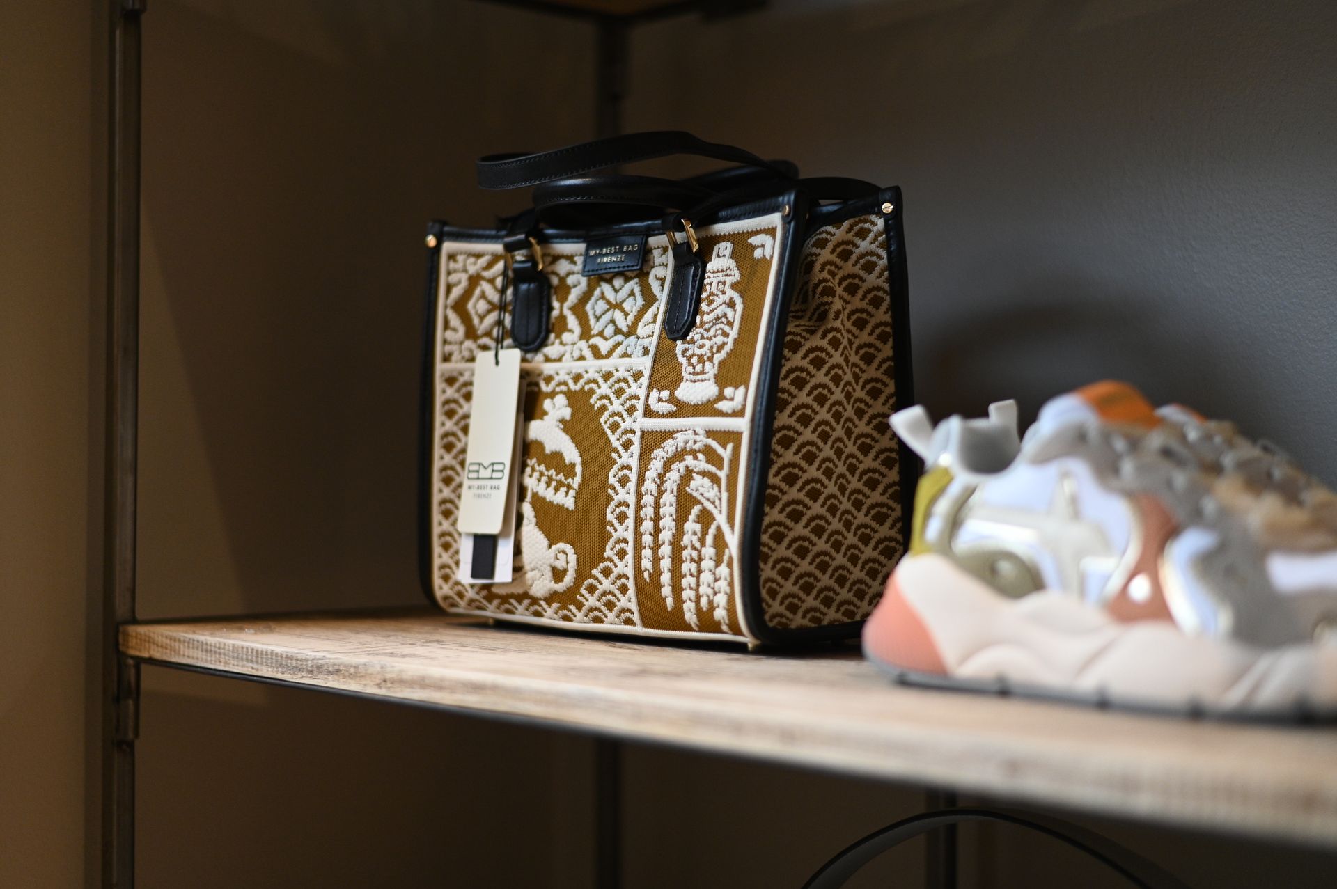 Borsa tote con fantasia marrone chiaro e marrone con etichetta su uno scaffale, accanto a una scarpa da ginnastica.