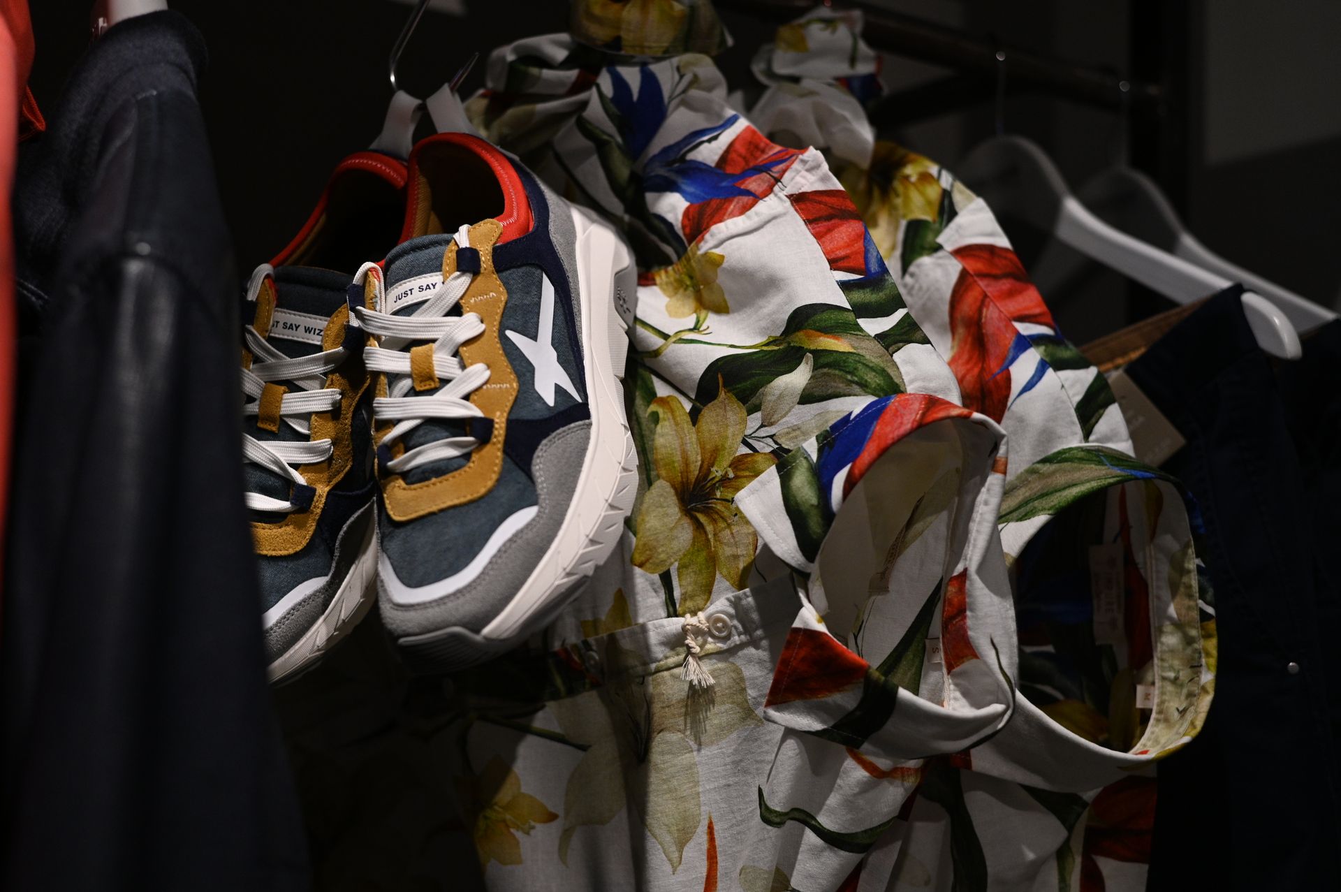 Scarpe da ginnastica e camicie floreali su un attaccapanni, con capi in pelle scura in bella vista.