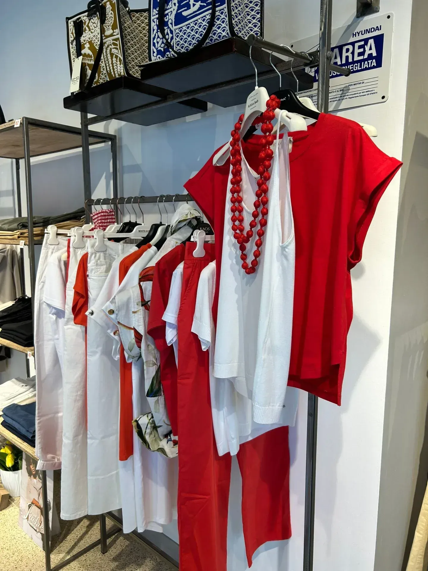 Appendiabiti in una boutique con abiti rossi e bianchi. Una collana di perline rosse è appesa a una canotta bianca.