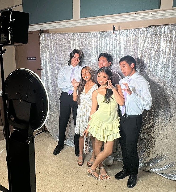 Four people posing in front of a silver backdrop at a formal event, smiling and holding drinks.