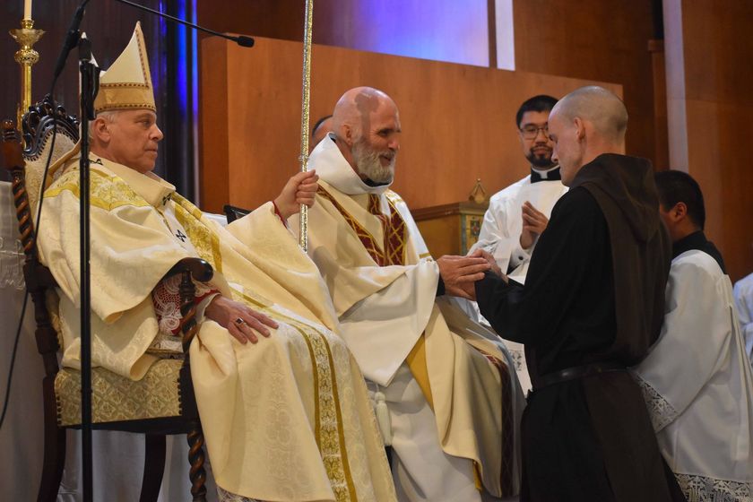 Clergy in white and gold robes seated during a religious ceremony, greeting a person in black in a church.