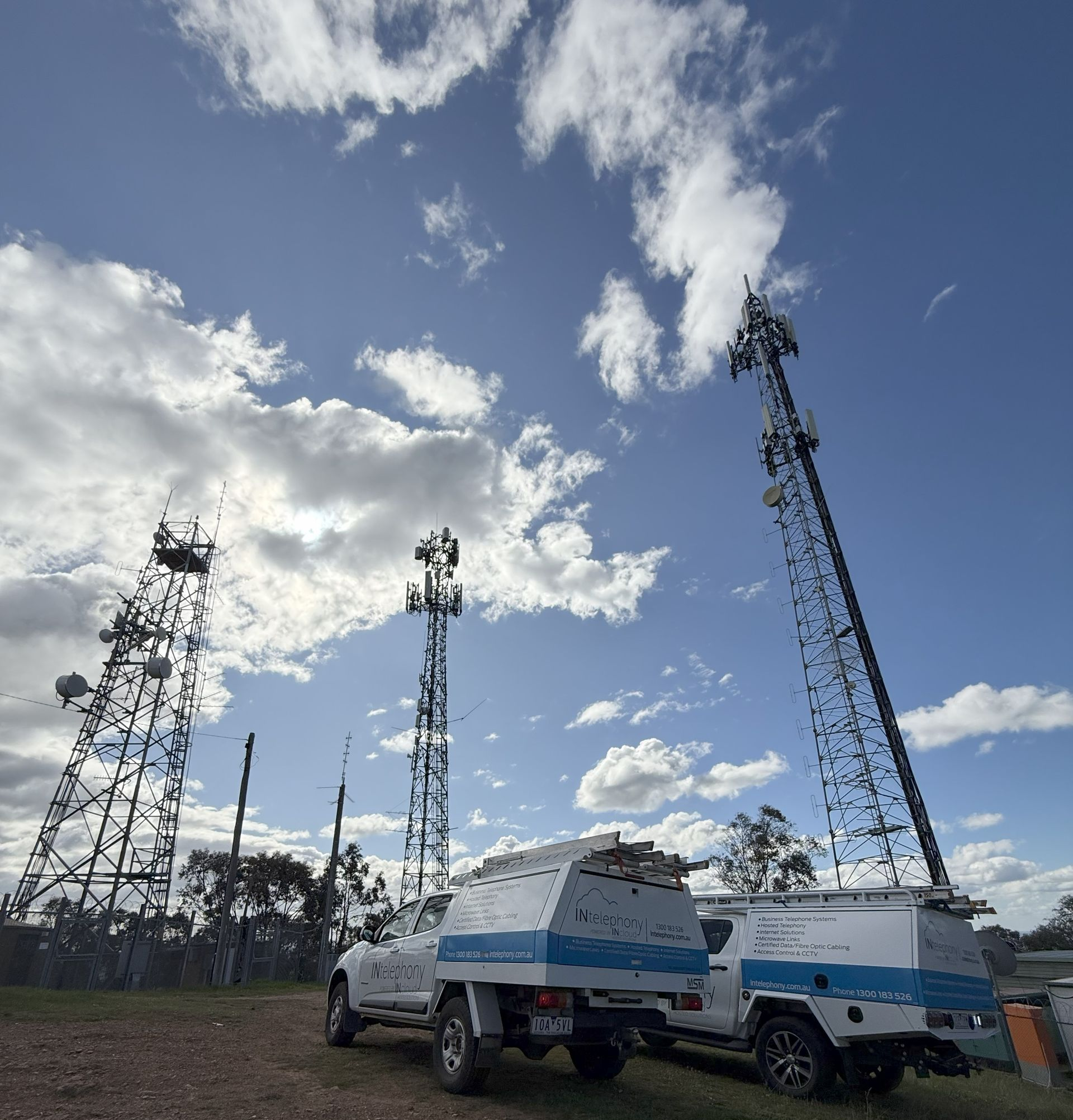 Three communication towers with white vehicles parked below, under a cloudy blue sky — INtelephony In Albury, NSW